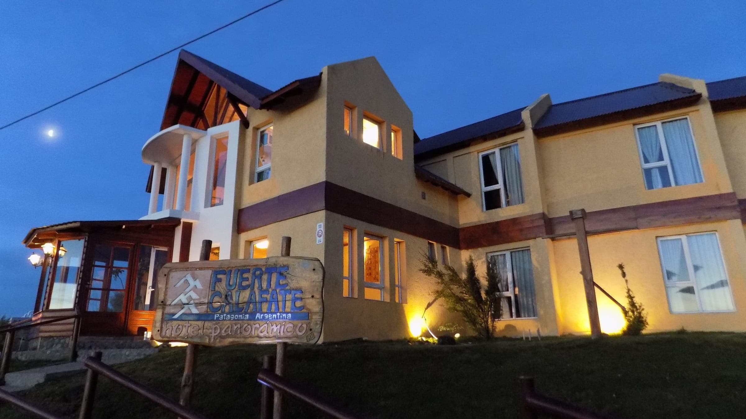 El hotel al anochecer, con las luces encendidas y el cartel de la entrada