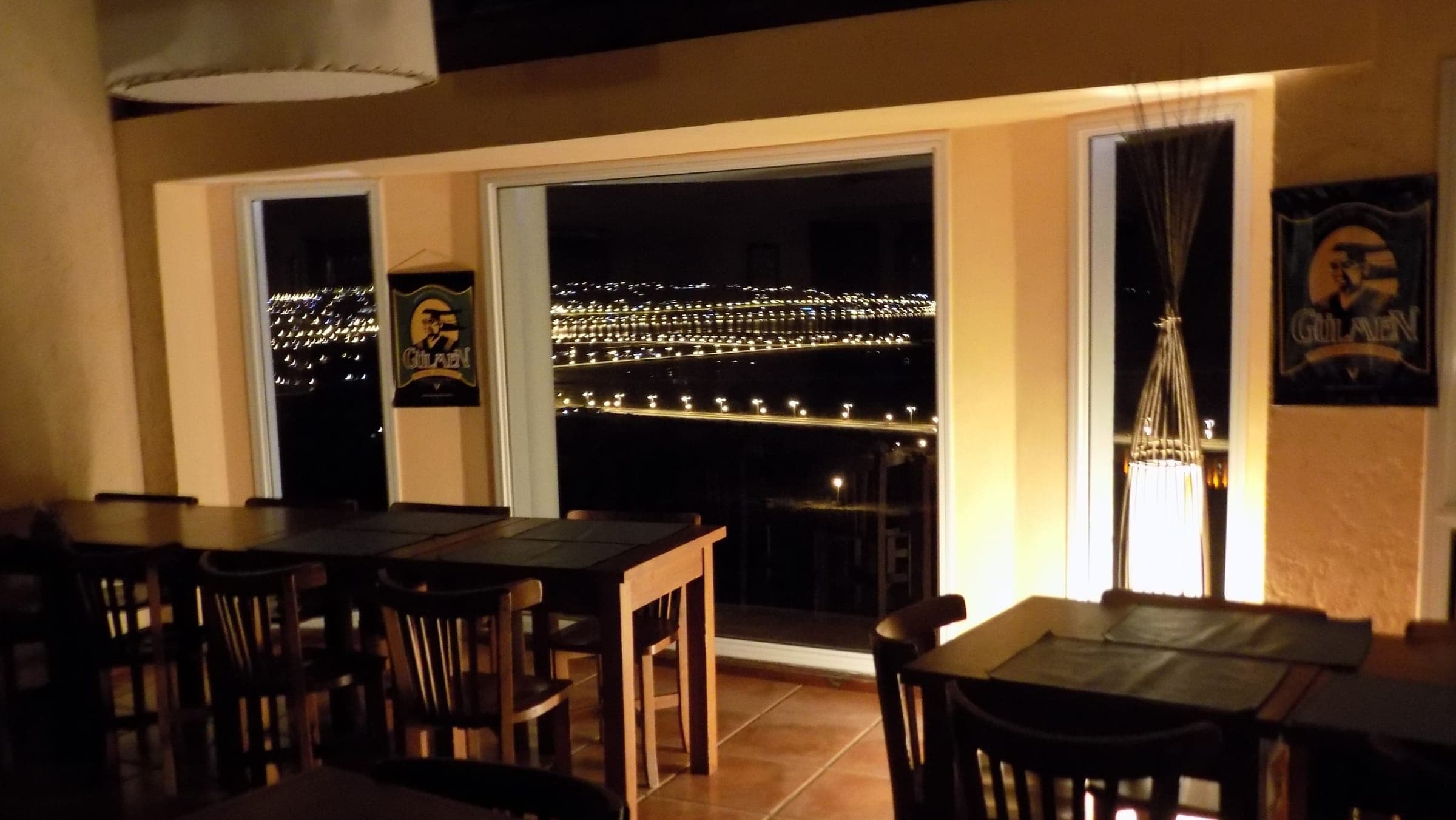 El restaurant de noche, con las luces del pueblo por el ventanal